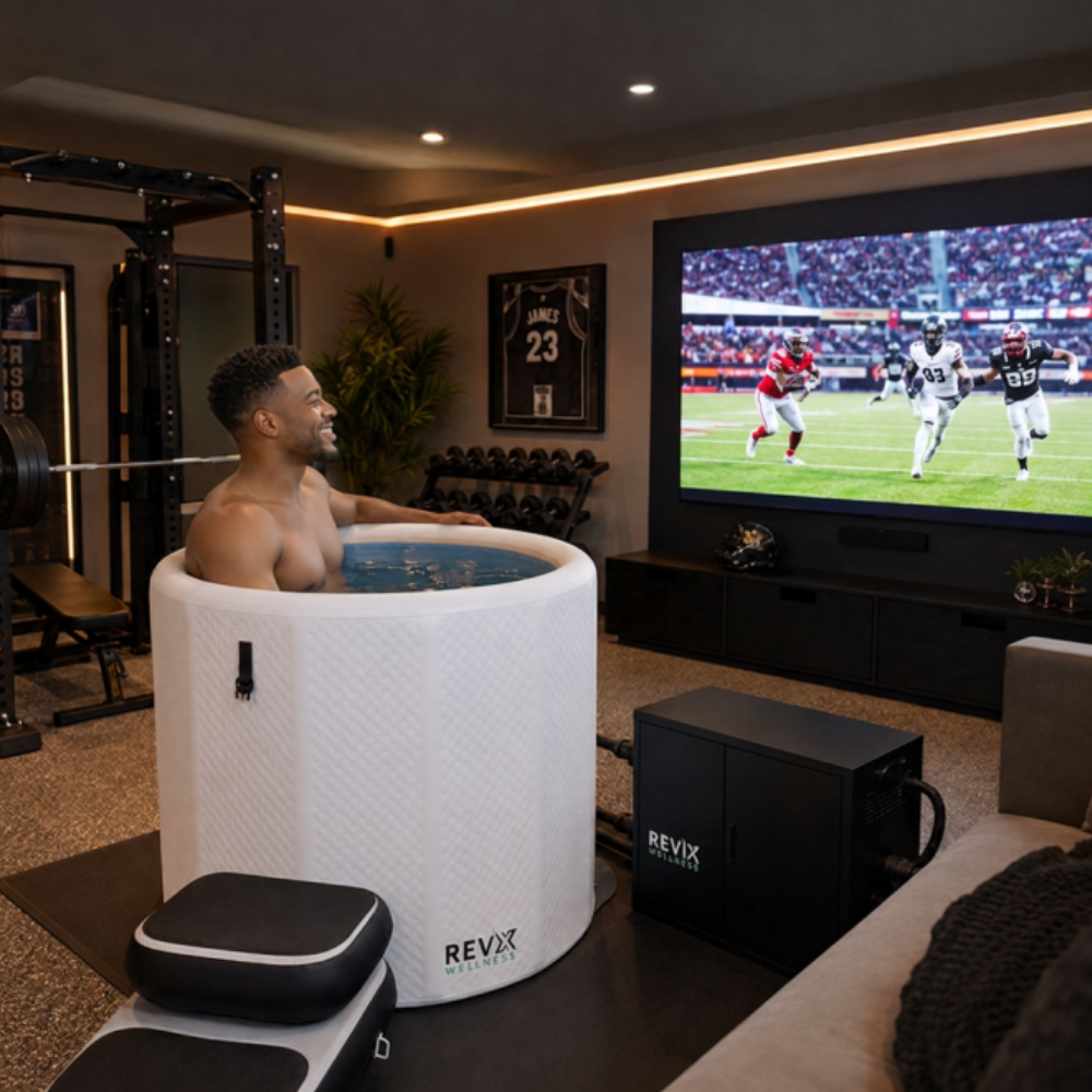 A man sits inside a white REVX RevX inflatable cold plunge barrel with insulated lid and inflatable entry steps in a modern home gym