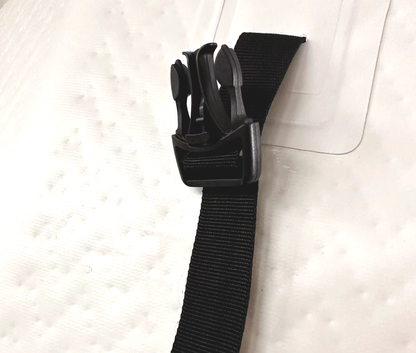 A close-up of a black nylon strap with a black plastic quick-release buckle, shown against a white textured RevX barrel